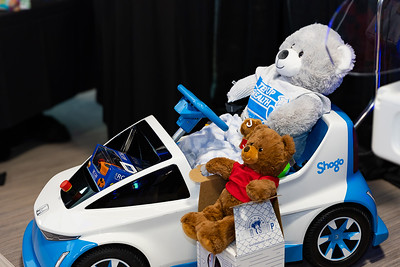 A toy car with a large teddy bear in the driver's seat, holding a small bear in a red shirt.