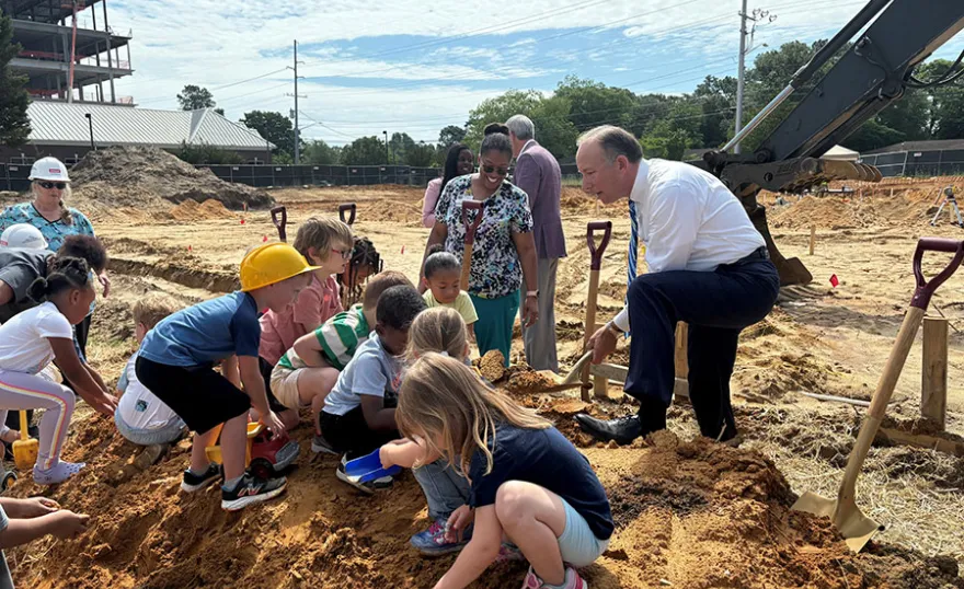 Mike Nagowski holds up shovel of dirt with some children at the groundbreaking.