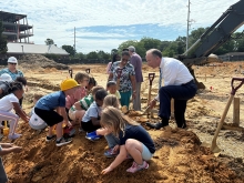 Mike Nagowski holds up shovel of dirt with some children at the groundbreaking.